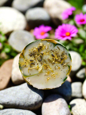 bar of soap with dried herbs flowers sitting on a rock sunny day
