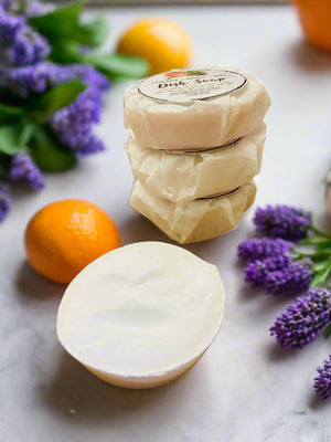 soap on shelf in kitchen near sink in sunny window in kitchen flowers and herbs in background with a kitchen towel lavender mint and oranges