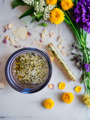Bath salts in jar and test tube on bathroom counter with flowers herbs and candle